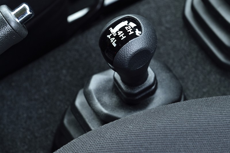 水平基調としたジムニーのインテリア。グローブをしたままでも操作しやすいような大型の集合スイッチやエアコンダイアルを採用。運転席と助手席の間には副変速機をレイアウト