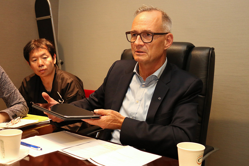 手元にあった紙資料を曲げた模擬の路面バンプとタブレットを使い、マジックボディコントロールとDYNAMIC BODY CONTROLサスペンションの違いを解説するフリュー氏