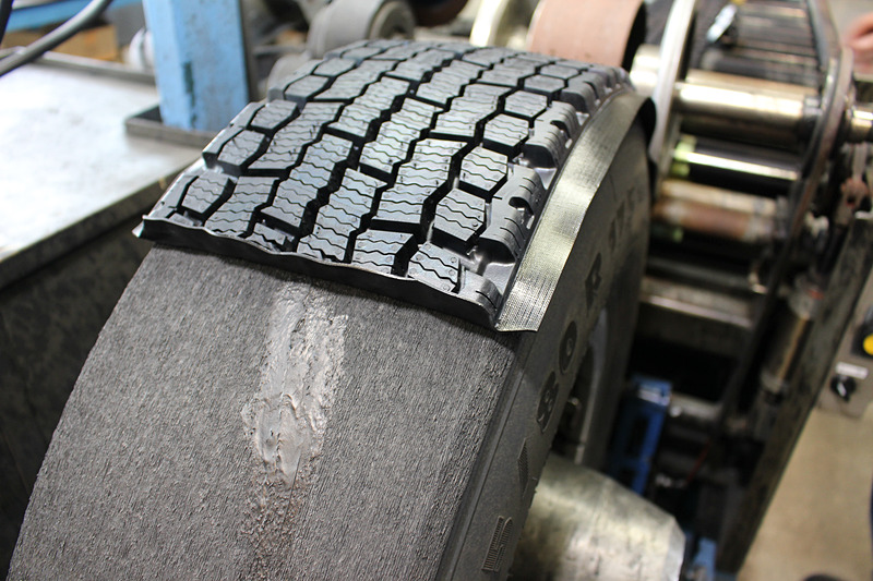 タイヤを回転させながらトレッドゴムを貼り付け、カットされたトレッドパターンの断面が両端で合うよう見極めながら作業が進められている