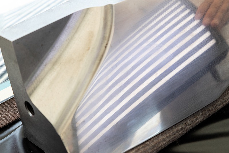 金型の検品イメージ。わずか数十ミクロンの誤差でも、蛍光灯で照らした反射が歪むことで判別できる。もちろん、こうなった金型を修正なしに使うことはないとのこと