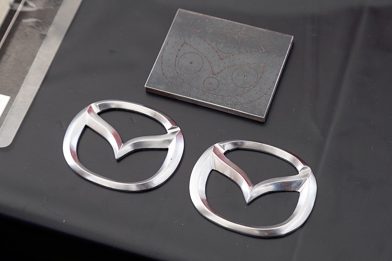 マツダのエンブレムの削り出し展示。右は少し学んだ程度の新人、左はベテランが手がけたもの。ベテランには敵わないが、新人でもこれだけでできることがすごい