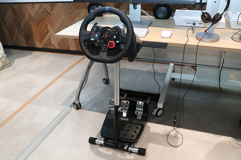 遠隔運転担当者の席にはPCとワイドディスプレイに加え、ゲーム用のステアリングコントローラーを設置。ディスプレイの表示はクルマの運転席を模して、中央に大きく車両正面を表示するほか、上側に車両後方、両サイドにドアミラーのように車両側面、右上にメーターパネルが映し出されている