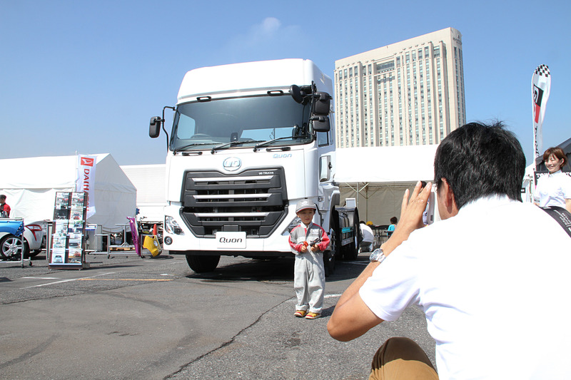 UDトラックスのブースでは、子供用のつなぎを着用して大型トラック「クオン」の前で記念撮影ができる。この写真をハッシュタグ「#UDキッズメカニック」をつけてインスタグラムに投稿すると、クオンのミニカーがプレゼントされるキャンペーンも展開している
