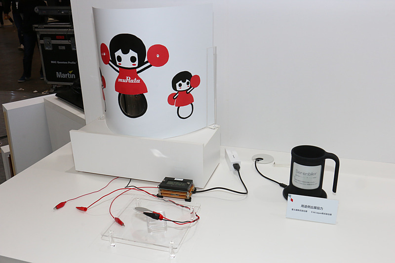 全固体薄膜電池の製品デモ。半円状に曲げられた全固体薄膜電池からの電力で、「村田製作所チアリーディング部」が持つポンポンのLEDライトが点滅している