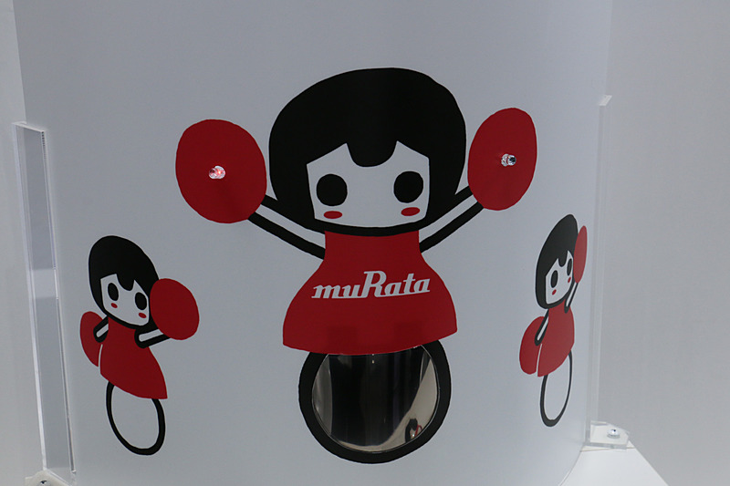 全固体薄膜電池の製品デモ。半円状に曲げられた全固体薄膜電池からの電力で、「村田製作所チアリーディング部」が持つポンポンのLEDライトが点滅している