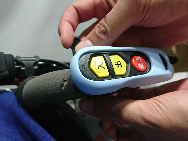 S字フックを車いすの左右に取り付けたあと、牽引ロープの作動リモコンを車いすのハンドルに装着し使用する