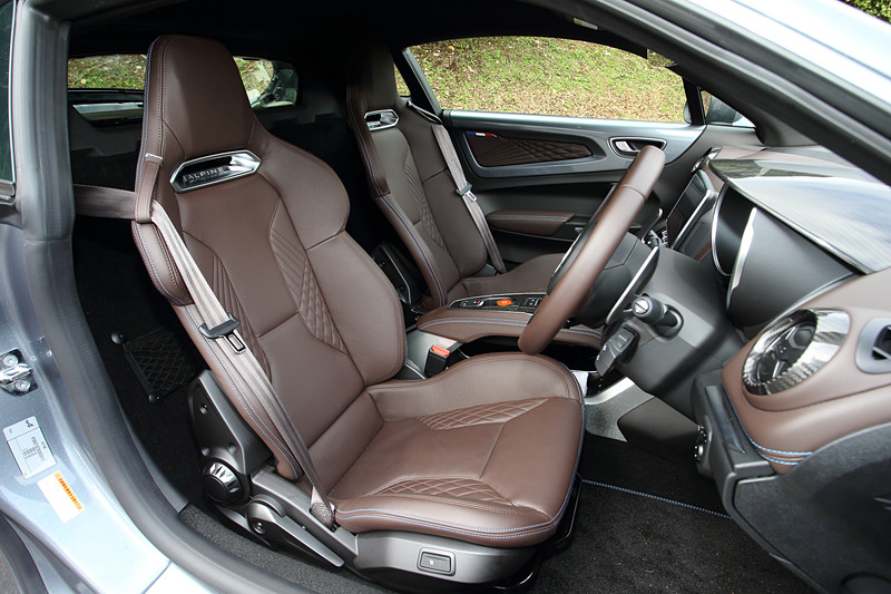 ブリリアントカーボン/アルミ/レザーを組み合わせるリネージグレードのインテリア。ブラウンレザーのSabelt製スポーツシート（シートリフター・リクライニング、シートヒーター付き）のほか、レザーステアリング/ブラックステアリングセンタートリム、FOCAL製軽量4スピーカー＋サブウーファーなどが専用装備になる