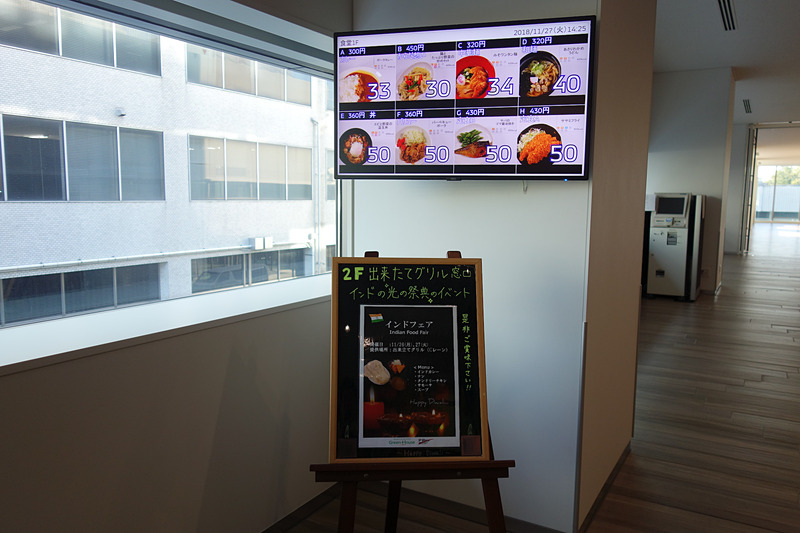 2階の食堂では食事する人数に合わせてさまざまな形状のテーブルが用意される。モニターにはメニューとともに残数の表示も。ユニークなのはフロアに書かれた英数文字。この日はAメニューが「カレー」（300円）だったが、「A/56」と書かれたところは「カレーに56人が並んでいます」という意味。ひと目で何のメニューにどれくらいの人が並んでいるかが分かるようになっている