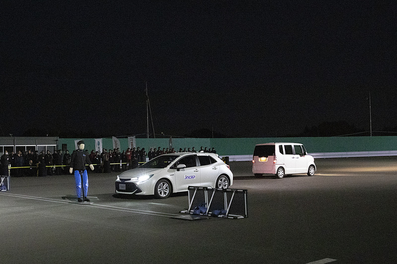 テストコースに移動して、対歩行者被害軽減ブレーキ（夜間街灯あり）デモンストレーションを実施。写真のようにヘッドライトを点灯した対向車がいる状態で40km/hで進行。対向車の影から歩いてくるダミーと衝突せずに止まれるかをチェックする。試験車はトヨタ カローラ スポーツ