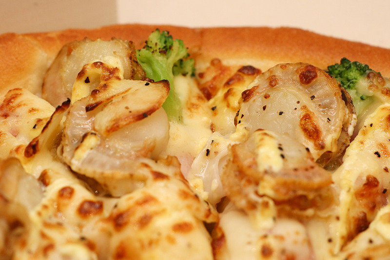 ピザハット代々木限定ピザの贅沢クリーミーホタテ。帆立、イカ、ベーコン、ブロッコリー、ガーリックを乗せ、ホワイトソースと特製マヨソース、ブラックペッパーを使用。柔らかな帆立がふんだんに使われ、ふんわりと香るガーリックで身体も温まる冬ならではのメニューだ
