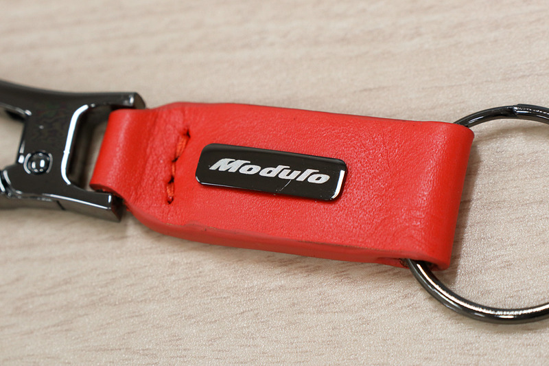 オレンジのレザーとクロームメッキのリングなどを組み合わせたキーチェーン。中央にModuloロゴの入ったクロームメッキプレートも備える