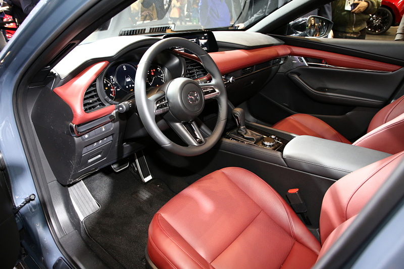 ハッチバック専用色となる「ポリメタルグレーメタリック」に塗装された新型Mazda3 CUSTOM STYLE（北米仕様ベース）。インテリアカラーはバーガンディで、マツダの新たな世界観を表現。エクステリアでも専用のエアロパーツを装備していて、ステージに飾られた「ソウルレッドクリスタルメタリック」や「マシーングレープレミアムメタリック」の新型Mazda3とは異なったテイストを醸している