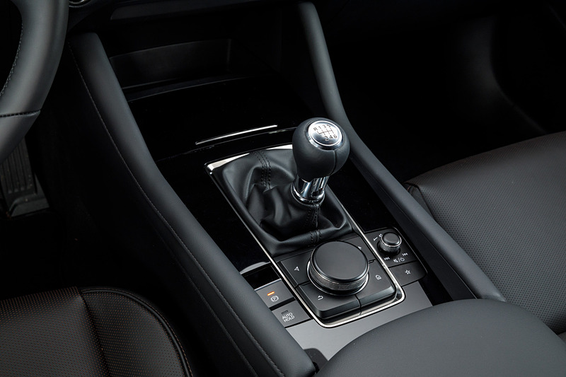 5ドアハッチバックのインテリア。新型Mazda3のコクピットはすべてをドライバーを中心に左右対称にレイアウト。ステアリングスポークやセンターディスプレイなど、パーツ単位で「バニシングポイント」（遠近法で言う収束点）に基づいてデザイン。また、本革にはマツダ独自のシボを採用したほか、シフトパネルにはレーザー加工で柄を刻み込んだ黒のメタリック層と、まっすぐ光を透過・減衰させるカラークリア層からなる2層成形と呼ばれる技術を採用