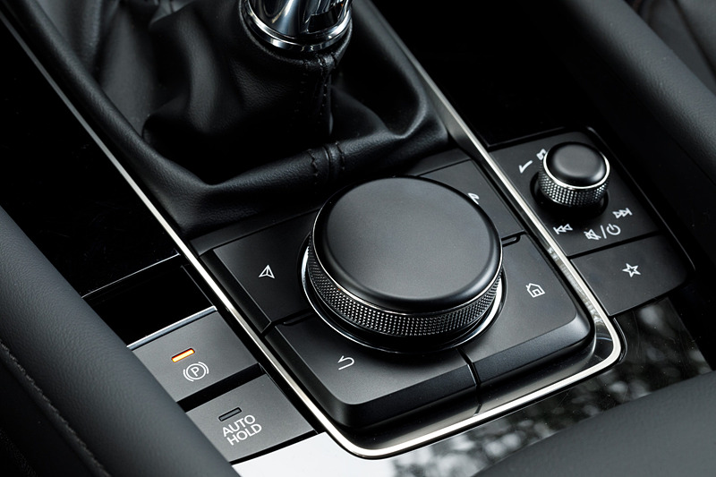 5ドアハッチバックのインテリア。新型Mazda3のコクピットはすべてをドライバーを中心に左右対称にレイアウト。ステアリングスポークやセンターディスプレイなど、パーツ単位で「バニシングポイント」（遠近法で言う収束点）に基づいてデザイン。また、本革にはマツダ独自のシボを採用したほか、シフトパネルにはレーザー加工で柄を刻み込んだ黒のメタリック層と、まっすぐ光を透過・減衰させるカラークリア層からなる2層成形と呼ばれる技術を採用