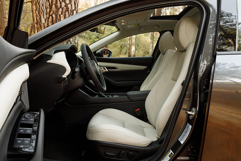 4ドアセダンのインテリア。5ドアハッチバックともどもマツダらしくドライビングポジションにもこだわり、ステアリングのテレスコピック量を前後10mmずつ拡大し、合計で70mmの調整幅を持たせることで体格に応じたドライビングポジション調整の精度を高めた。シフト位置は現行モデルに対してAT/MTともに前方・上方に移動させ、ステアリングからの持ち替えのしやすさとシフト操作のしやすさを向上させたという