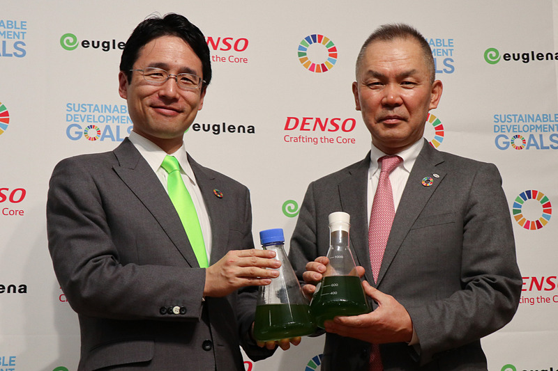 共同発表会でそれぞれの会社で生産している微細藻類の培養液を手にフォトセッションに立つ株式会社ユーグレナ 代表取締役社長 出雲充氏（左）と株式会社デンソー 専務役員 伊藤正彦氏（右）