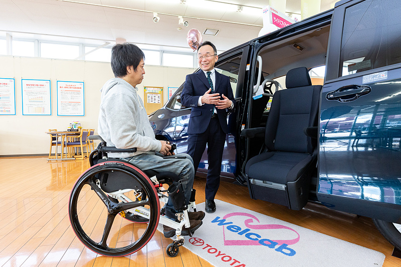 「助手席リフトアップシート」との比較で、シートがチルトすることによりお尻の位置を高く保て、地面に両足が着き、足を浅く曲げた状態から前に乗り出すので、立ち上がりやすいといった「サイドリフトアップチルトシート」の特徴を紹介する中川氏