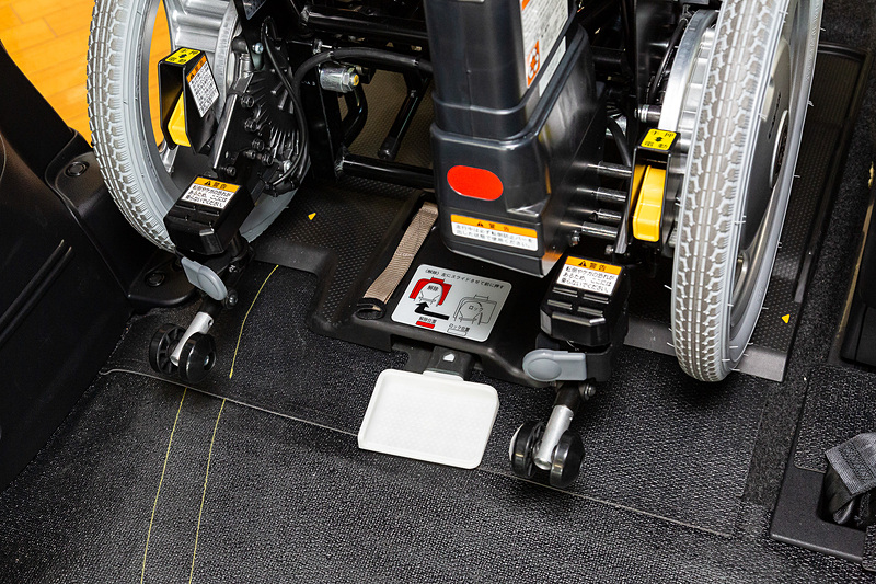 車いすのリリースは、介助者が足で白い板を左に動かして前に押す2アクション式。これは車内の揺れで動いた荷物などが当たり、ロックが解除されるのを防ぐため