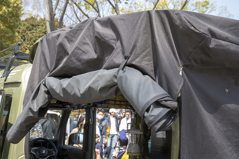 テールゲートカーテン（2万3760円）は開いたテールゲートに被せる簡単装着でプライベートルームが作れる。カーテンのバタ付き防止に水入りペットボトルを入れるポケットもあり、左右はジッパーで開閉して巻き上げておける作り