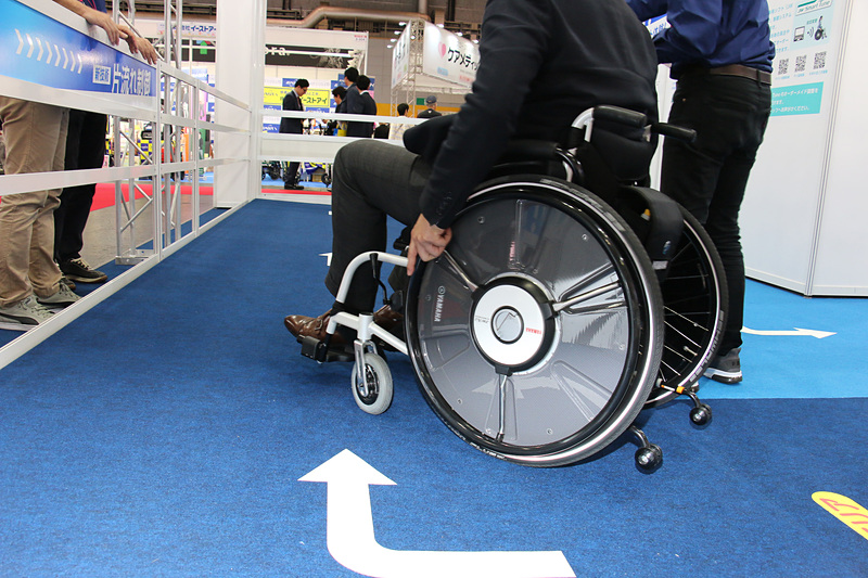 右肩下がりに設定された特設スペースでJWスウィングの体感試乗を実施。「片流れ制御」をOFFにした状態では、とくに若い男性などが乗っているとアシストが働きすぎてしまい、怖いぐらいの勢いで車いすが右旋回していく。これをモーターアシストの補正で直進させるのが片流れ制御となる