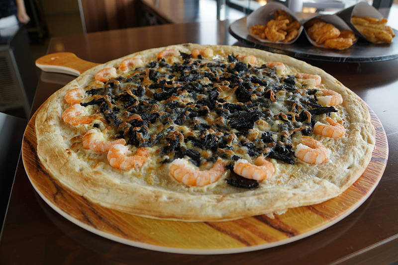 COURSE SIDE PIZZERIA -GRAN VIEW-ではさまざまな種類のピザが提供される。写真は鈴鹿サーキットのお土産として人気の「タイヤカスさきいか」とイカスミソースを使用した「タイヤカスブラック」（8分の1カットで提供される）