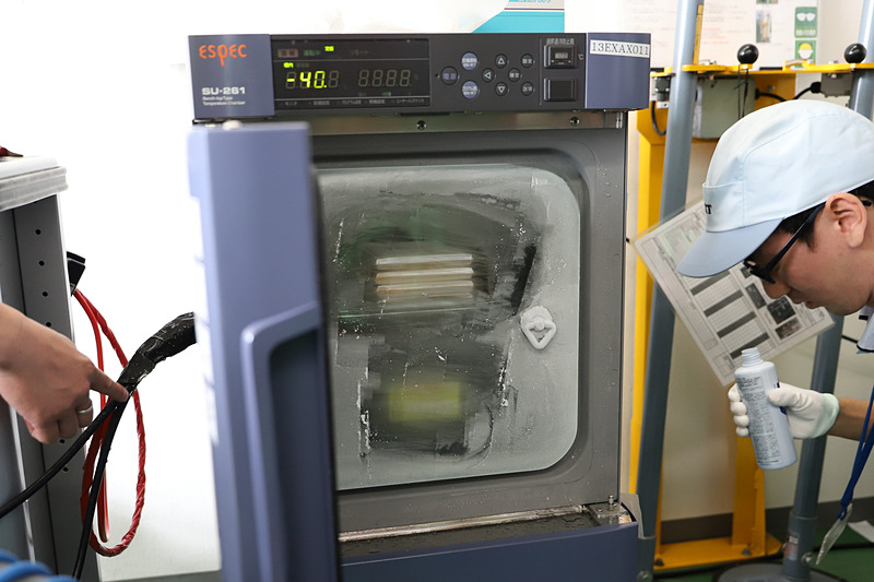 特殊な機械の中で-40℃になるように冷やされた高耐熱リチウムイオンキャパシタ（上）と純正バッテリー（下）。表面の霜を拭いてもすぐにまた霜がついてしまうくらい、キンキンに冷やされていた。なお、デモンストレーションに使用した純正バッテリーの動作保証温度は約-30℃とのこと