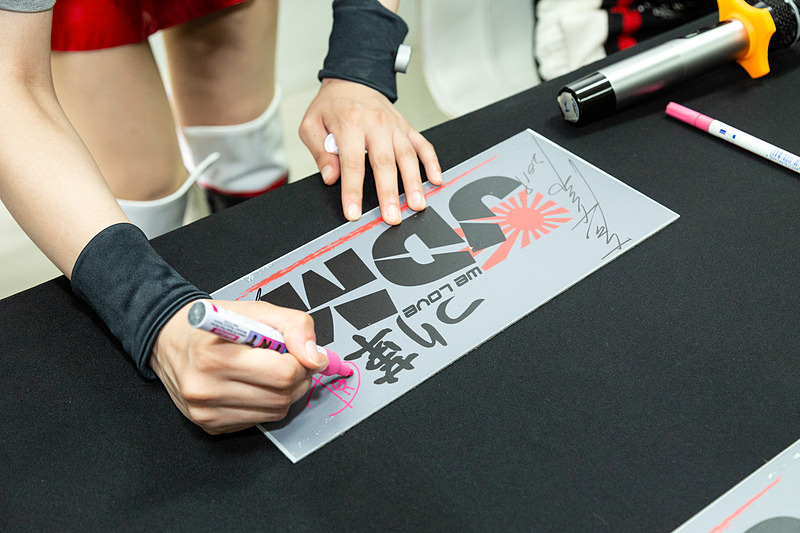 4人がステージに並び、参加者が持ってきた思い思いのグッズにサインしていく