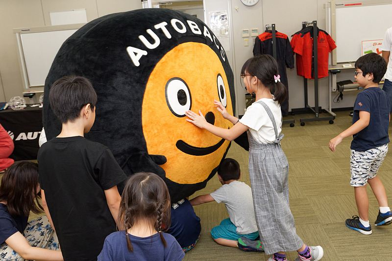 オートバックスのマスコットキャラ「タイヤくん」と遊ぶ子供たち
