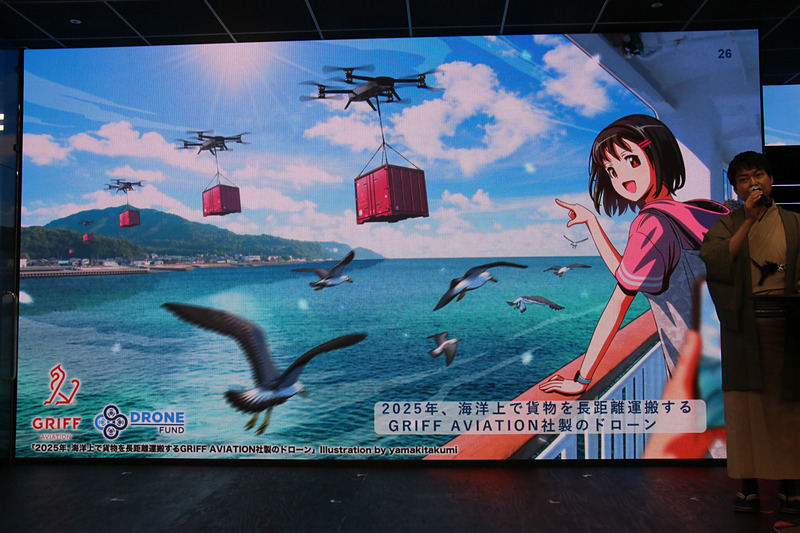 ドローンによる荷物の運搬はさらなる重量物にも対応できるよう開発が進められ、例として災害時の救助をイメージして人間相当の重量物を運ぶシーンが紹介された