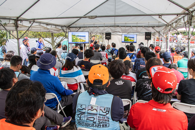 2台のモニターが設置されたブース内の様子。用意された椅子は満席となり、左右には立ち見の参加者も多数