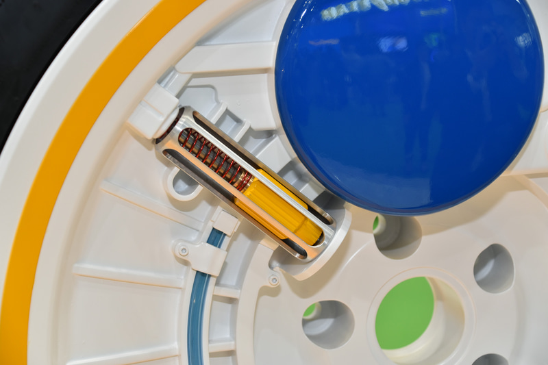 遠心ポンプのクローズアップ。遠心力でピストンが外側に振りまわされることで、空気が空気リザーブタンク（青く丸い部位）に送られる。遠心力が弱まるとバネがシリンダーを押し戻す。なお、吸入される空気はそのままホイール外の外気から取り入られる