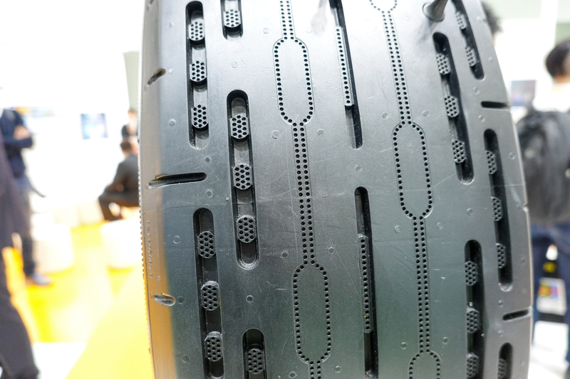 今回展示されていたConti C.A.R.E.対応コンセプトタイヤは横溝がないことも特長として挙げられていた。これは自動運転×電動ベースのバスやタクシーでは最高速がそれほど高くならないため。縦溝のみにすることで転がり抵抗が低減され、電費の向上に貢献する。また、縦溝の中に空いている「無数の微細穴付き突起」はロードノイズを低減させる役割を果たす。具体的には、凹部に溜め込まれた衝撃音を、この無数の微細穴付き突起構造によって拡散することで低減している