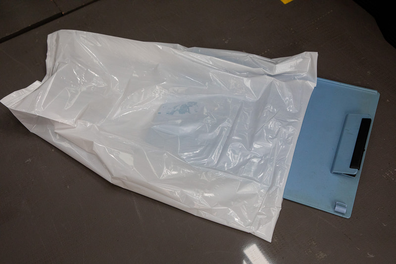 A4サイズのクリップボードとの比較。レジャー先で出た生ゴミなどの持ち帰る用途にも使えるので、BOSもアウトドアレジャーでは持っていった方がいいアイテムだ。なお、BOSは燃やしても有害なガスが出ないので、凝固剤などを使用して水分を固めておけば燃えるゴミとして出すことができる（自治体ごとのゴミ出しの決まりは要確認）