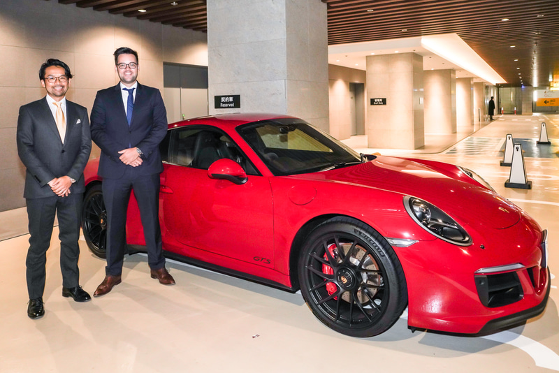 ポルシェ公式プレミアムレンタカーサービス「ポルシェ・ドライブ」で受け渡し場所となる虎ノ門ヒルズ地下2階にて。ポルシェジャパン株式会社 コーポレートビジネスディベロップメント 担当部長 アンドレ・ブランド氏（右）と同スマートモビリティ担当 富永憲英氏（左）