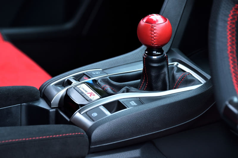 上下はドライカーボン、左右はパンチングレザーを採用し、スポーティかつ高いフィッティングにより安定感のある操作性を実現するスポーツステアリングホイール(8万9100円)。ショートストローク化と、ドライバー側へシフト位置をオフセット。リターンスプリングの変更および、マウントブッシュを排したリジッドマウント化と併せて節度感をさらに高め、確実かつ素早い操作性のシフトフィーリングを実現。クイックシフター(3万6300円)。カーボン製シフトノブ(1万9800円)。アルミ製シフトノブ(1万780円)。写真はアルミ製×本革巻きシフトノブ(1万7600円)。エンジンスタータースイッチ(1万9800円)