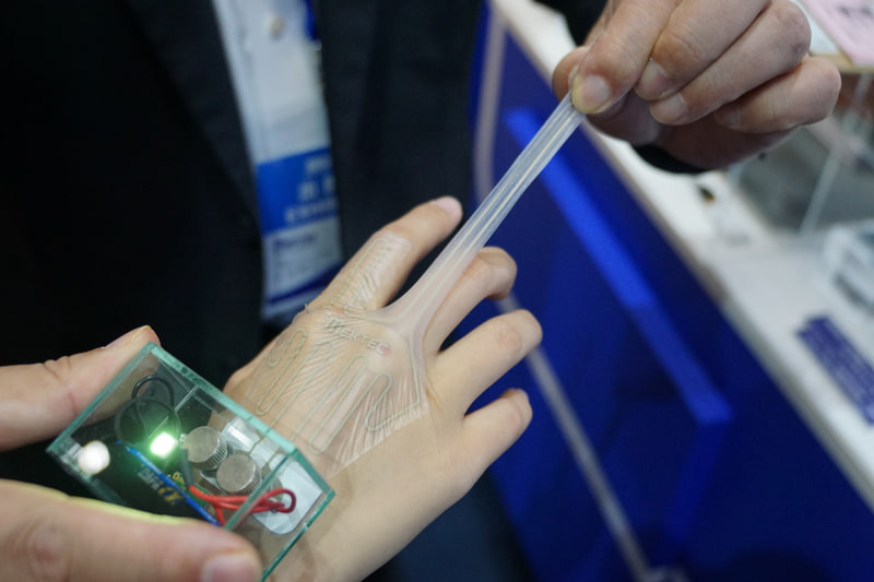 NOKブース。伸縮FPCは通気性があり伸びた状態でも通電。導電体を印刷することでコストを抑え使い捨てを可能にしている