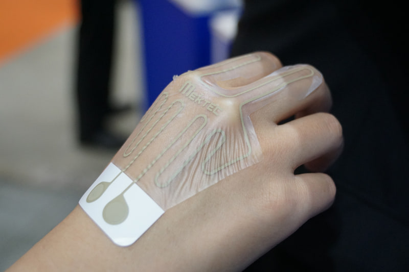 NOKブース。伸縮FPCは通気性があり伸びた状態でも通電。導電体を印刷することでコストを抑え使い捨てを可能にしている