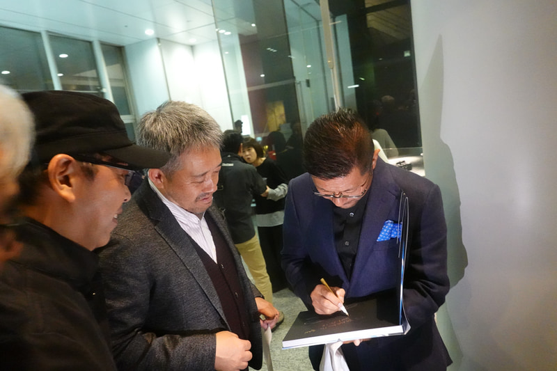 写真集を購入した山本氏の要望に応えてサインする熱田カメラマン。「山本さんにはプレゼントしますよ」（熱田）、「いいんだよ、オレは買いたいんだよ」（山本）という会話がなされていた