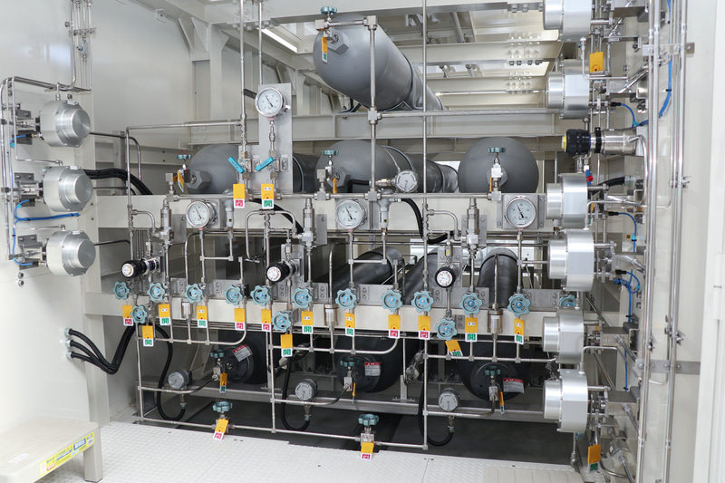 充填前の圧縮された水素を保管する「蓄圧器」。7本並ぶタンクの内、下段の3本が82MPaに対応。上段の4本は40MPaの対応品。このほか、40MPaのタンク9本が並ぶ予備も用意されている