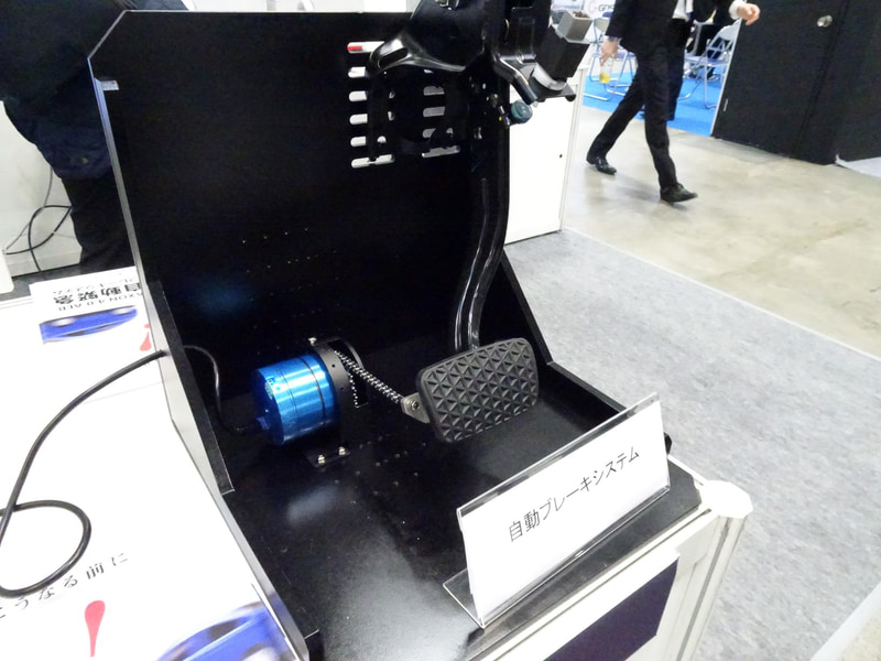 ペダルのアームをモーターで引っ張り上げる簡易型。韓国では50台のバスとタクシーに装着して実証実験を行なっているという。ミリ波レーダーと光学式カメラを用いてTTC（衝突予測時間）の2秒前に警告、1.6秒前に弱いブレーキ（アームを少し引っ張る）、1秒前に強いブレーキ（アームを力いっぱい引っ張る）ことで機能させる