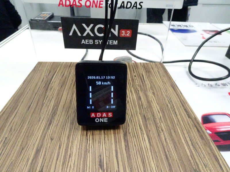 ペダルのアームをモーターで引っ張り上げる簡易型。韓国では50台のバスとタクシーに装着して実証実験を行なっているという。ミリ波レーダーと光学式カメラを用いてTTC（衝突予測時間）の2秒前に警告、1.6秒前に弱いブレーキ（アームを少し引っ張る）、1秒前に強いブレーキ（アームを力いっぱい引っ張る）ことで機能させる