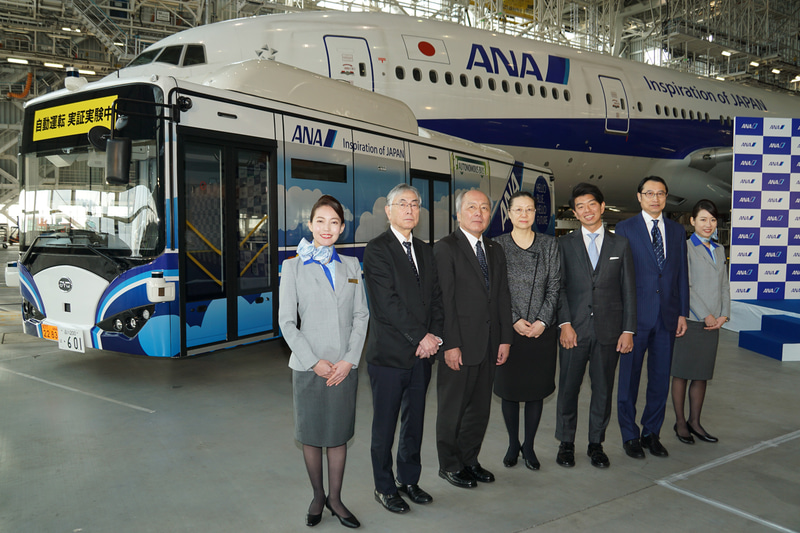 2名の客室乗務員に囲まれた式典出席者による記念撮影。左から先進モビリティ株式会社 代表取締役社長 青木啓二氏、全日本空輸株式会社 代表取締役 専務執行役員 清水信三氏、来賓の中華人民共和国 駐日本国大使館 公使 郭燕氏、SBドライブ株式会社 代表取締役社長 兼 CEO 佐治友基氏、BYD アジア太平洋地域 自動車販売事業部 総経理 ビーワイディージャパン株式会社 代表取締役社長 劉学亮氏