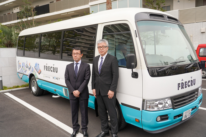 FRECRU用の車両を前に記念撮影する日鉄興和不動産株式会社 常務取締役 住宅事業本部長 吉澤恵一氏（左）とMONET Technologies株式会社 代表取締役副社長 兼 COO 柴尾嘉秀氏（右）