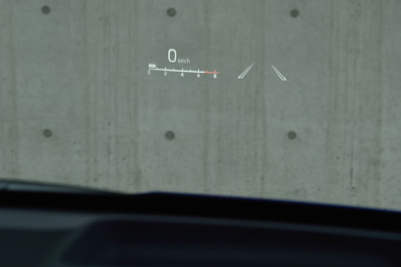 ヤリス（上）とMAZDA2（下）に座ってみたところ。時間が経過するにつれ、シートに対する印象が変わった。ウィンドウに直接投影するヤリスは見た目にもスマート。だが、着座位置によってはウィンドウの歪みに投影した表示類が重なり認識率がわるくなる。一方、MAZDA2は透過度の高い樹脂パネルに投影する方式。慣れるまで視界が部分的に遮られたような感覚になるが、文字は細部に至るまでくっきり。悪天応にも邪魔されない