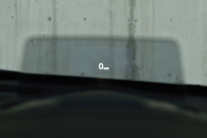 ヤリス（上）とMAZDA2（下）に座ってみたところ。時間が経過するにつれ、シートに対する印象が変わった。ウィンドウに直接投影するヤリスは見た目にもスマート。だが、着座位置によってはウィンドウの歪みに投影した表示類が重なり認識率がわるくなる。一方、MAZDA2は透過度の高い樹脂パネルに投影する方式。慣れるまで視界が部分的に遮られたような感覚になるが、文字は細部に至るまでくっきり。悪天応にも邪魔されない