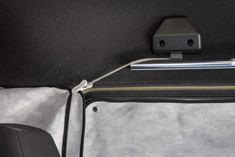 フロントプライバシーシェード両端を支えるため、クリップ（洗濯ばさみ）とゴムバンドを使った補強も入れてみた。ゴムバンドの反対側は純正アクセサリーのルーフインナーサイドパイプに引っかける。よりしっかり吊り下げられるようになった印象だ