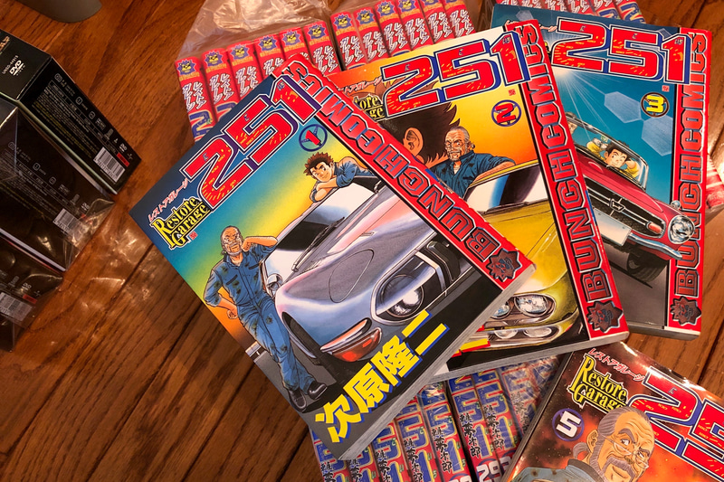 2001年に刊行された「レストアガレージ251（にこいち）」（次原隆二著）は、女好きだけど腕は一流の主人公・夢次郎のもとにやってくる、廃車寸前のボロ車とそこで交差する数々の人生たちが、笑いと涙を誘う物語。よぉ～く見ていると、現役で活躍するクルマ業界のカメラマンさんの名前とか、「おっ」と思える発見もあって楽しいですよ（笑）。左上にチラッと映っている大量のDVDも、夫が外出自粛を乗り切るために仕入れた懐かしいものなのですが……。それはまた別の機会にでもご紹介しますね