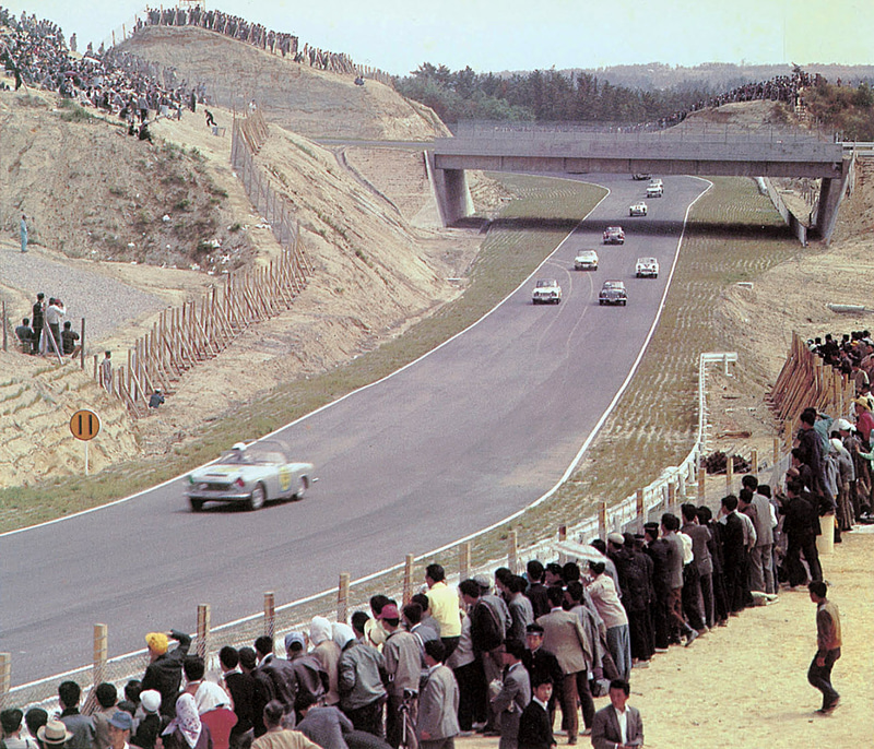 1963年、第1回日本グランプリ自動車レース、国内スポーツカーB IIクラス。ヘアピンのイン側に観客エリアがあり、立体交差の左上を見ると130Rの外側とデグナーのイン側の土手が高く観客エリアとなっている。デグナーのアウト側も切り立った崖でかなりの観客が見える