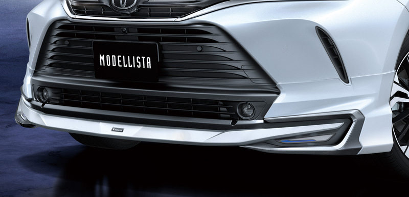 「フロントスポイラー（LED付）」（素地：9万7900円、塗装済：10万3400円）。センターからワイド方向に広がる造形に、左右のグレーメタリック加飾がコの字状に重なり、メカニカルでアグレッシブなスタイルを強調。クリアレンズに覆われたLEDイルミは、立体的に発光するホワイトの光とブルー加飾のアクセントにより、精密感のある先進的なイメージを演出する