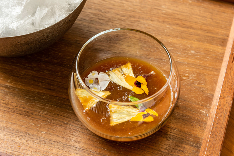 自家製ジンジャービアジェリーソース。国産ショウガを発酵させ、オーガニック黒糖のコクを合わせ作り上げた自家製ソース。ジンジャービアならではの大人の刺激が新鮮な味わいを提供。仕上げにエディブルフラワーを添えた。原材料：国産生姜（主に高知県産）、国産有機レモン（愛媛県・広島県産）、オーガニック黒糖、エディブルフラワー